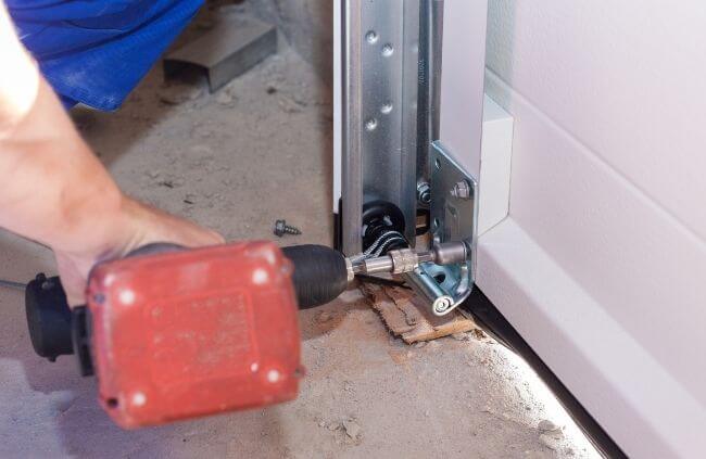 Garage Door Repair Guys performing garage door maintenance, tightening the lower roller bracket for smoother and safer door movement.
