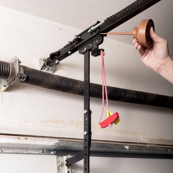 Garage door servicing, technician lubricating the track and opener components to improve performance and extend system lifespan by Garage Door Repair Guys